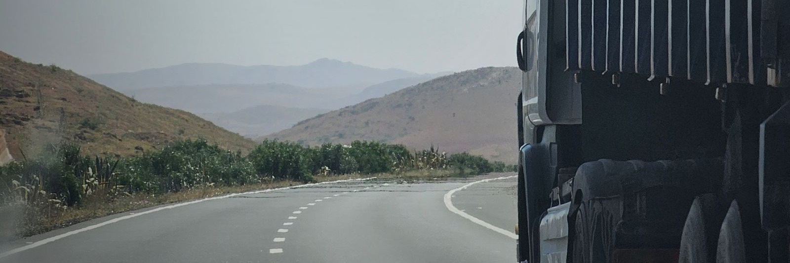 Fiancata telonata di un camion su una strada che curva fra colline aride.